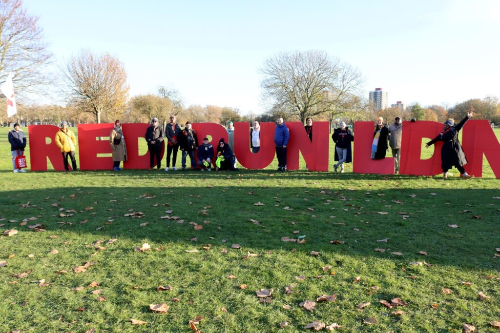 People standing next to big red letters in a grassy field that say "RED RUN".