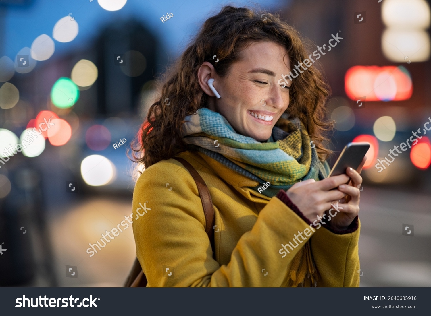 stock-photo-beautiful-woman-using-mobile-phone-while-listening-voice-note-with-wireless-earbuds-smiling-girl-2040685916