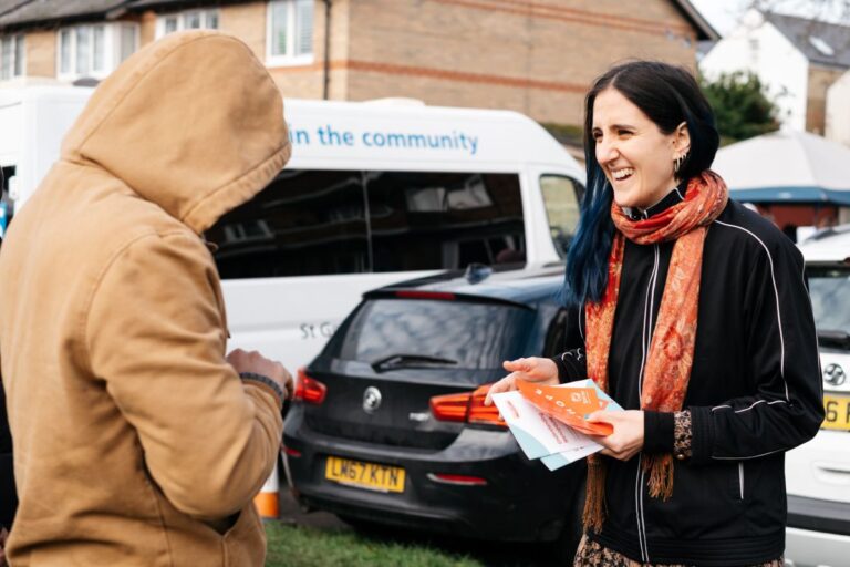 Two people talking outdoors, one of them holding some Spectra flyers.