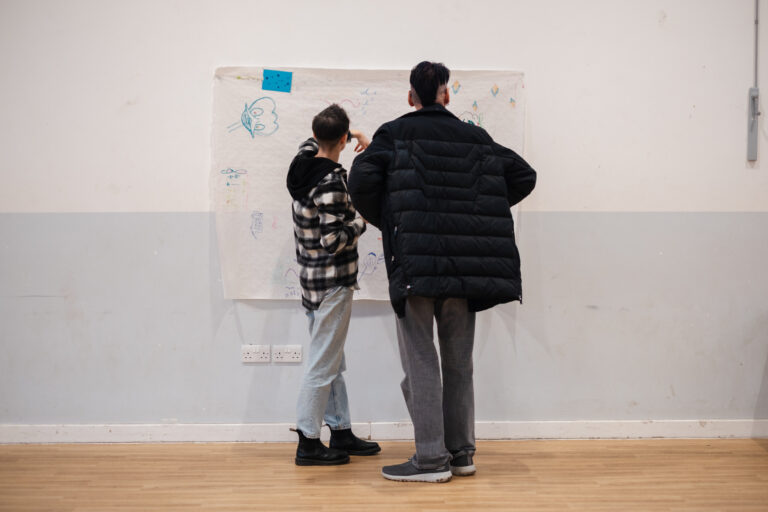 Two people, standing, writing something on a whiteboard on a wall.
