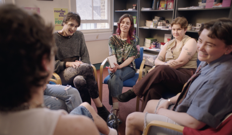 A group of people sitting in a circle, looking at one of them talking.