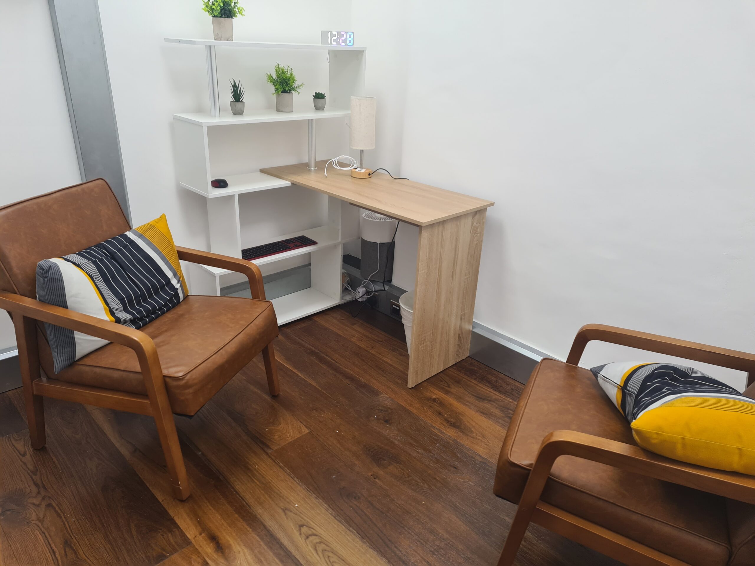 Close up of a small room with two armchairs, a small beige desk and a white bookcase