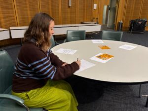 A person sitting on a chair by the table and writing on a piece of paper.