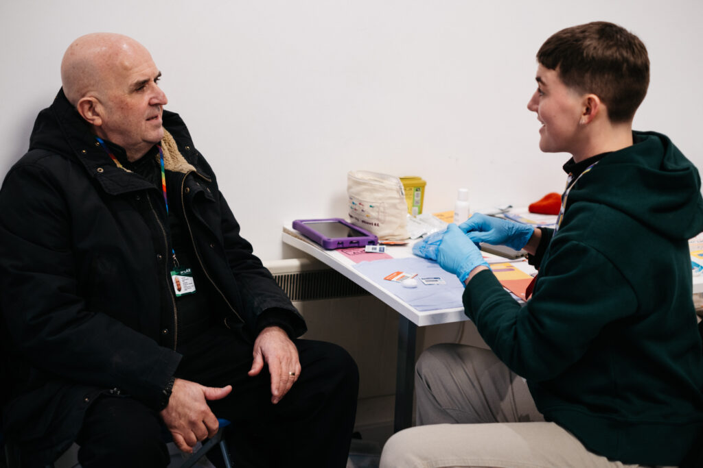 Two people chatting by a table, one of them wearing blue rubber gloves, preparing an HIV kit