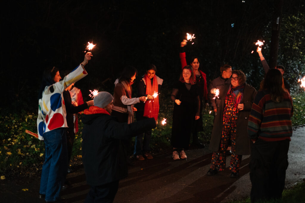 A group of people in the dark wearing winter clothes and holding sparklers.