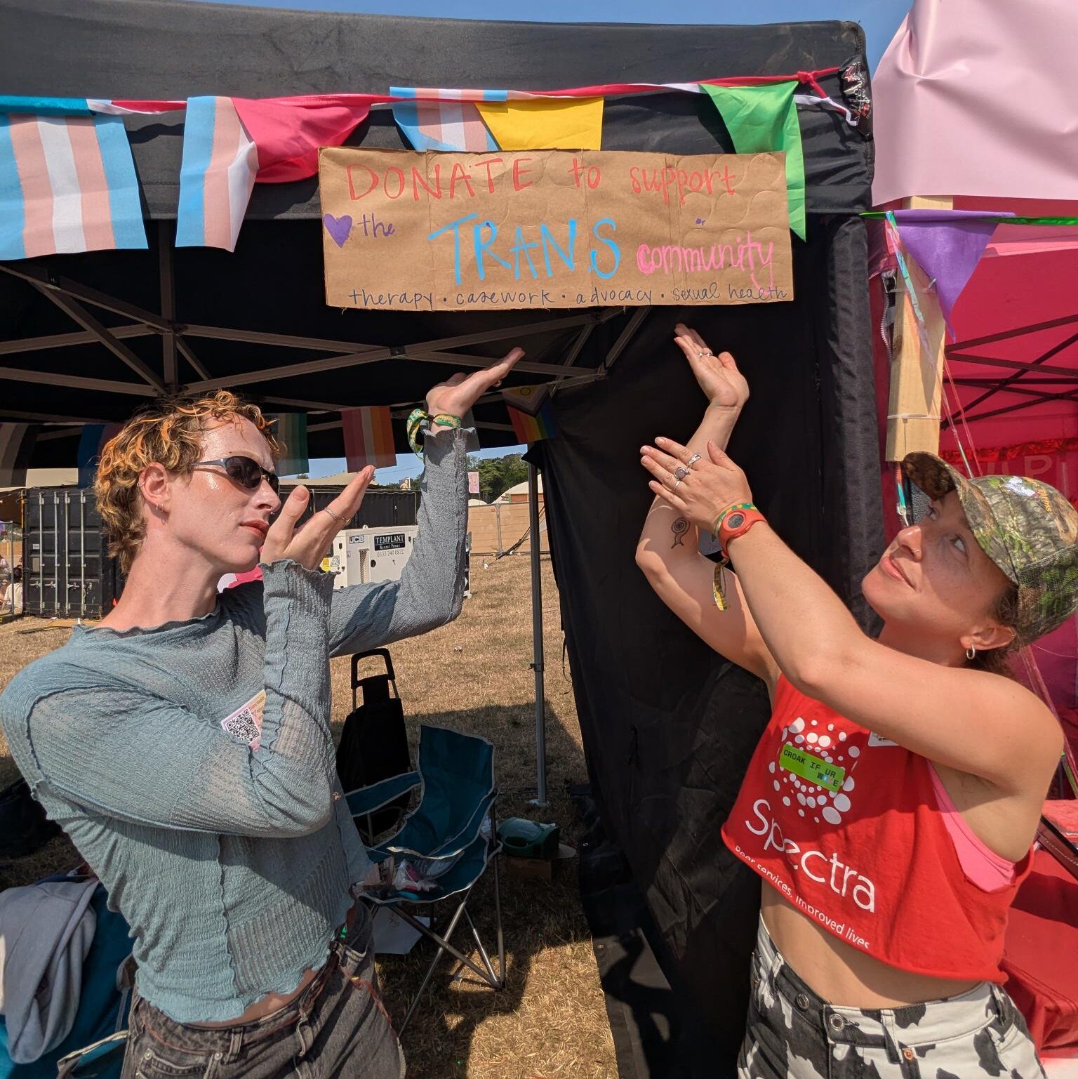 Two people playfully pointing at a banner about them that says 'Donate to Support Trans Community'
