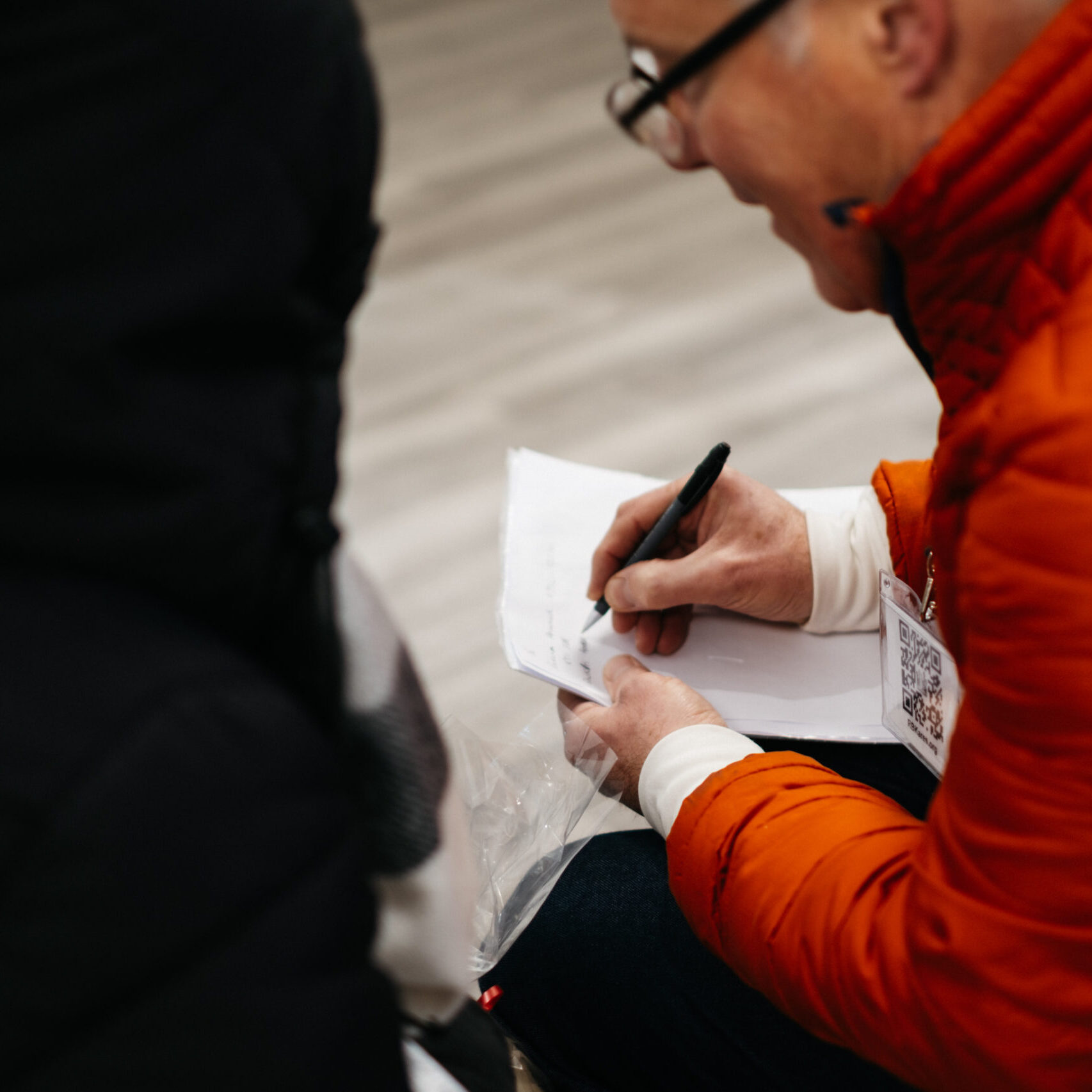 A person in a red jacket writing something on a piece of paper.