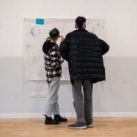 Two people, standing, writing something on a whiteboard on a wall.