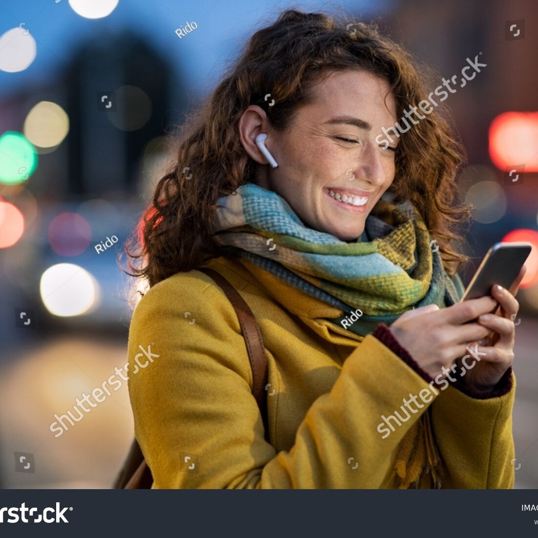 stock-photo-beautiful-woman-using-mobile-phone-while-listening-voice-note-with-wireless-earbuds-smiling-girl-2040685916